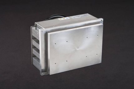 Three-quarter view of large thermoelectric cold plate cooler/heater incorporating six thermoelectric modules. The cooled aluminum plate on the front and waste heat is exhausted to high-density fins on the back. Fins are fan cooled. The fan air enters on the middle back and exhausts on sides. Operates on 24 volts DC and removes 204 watts of heat at a 0°C temperature difference relative to ambient. Internal extender blocks improve the heat pumping capacity at larger temperature differences. Can heat to 100°C without damaging the cooler.