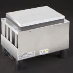 Three-quarter view of large thermoelectric cold plate cooler/heater incorporating six thermoelectric modules. The cooled aluminum plate on the front and waste heat is exhausted to high-density fins on the back. Fins are fan cooled. The fan air enters on the middle back and exhausts on sides. The cooler incorporates legs which lift the fan's air inlet off of a table top, so the cooler can be operated directly on a table. It operates on 24 volts DC and removes 204 watts of heat at a 0°C temperature difference relative to ambient. Internal extender blocks improve the heat pumping capacity at larger temperature differences. Can heat to 100°C without damaging the cooler.