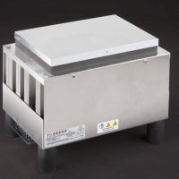 Three-quarter view of large thermoelectric cold plate cooler/heater incorporating six thermoelectric modules. The cooled aluminum plate on the front and waste heat is exhausted to high-density fins on the back. Fins are fan cooled. The fan air enters on the middle back and exhausts on sides. The cooler incorporates legs which lift the fan's air inlet off of a table top, so the cooler can be operated directly on a table. It operates on 24 volts DC and removes 204 watts of heat at a 0°C temperature difference relative to ambient. Internal extender blocks improve the heat pumping capacity at larger temperature differences. Can heat to 100°C without damaging the cooler.