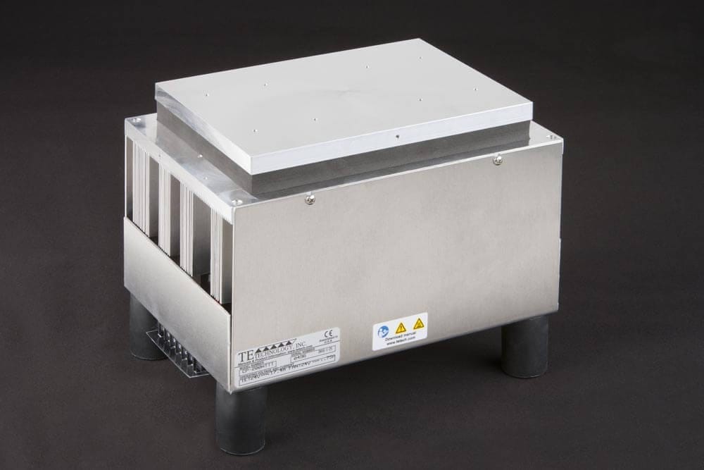 CP-200HTTT Three-quarter view of large thermoelectric cold plate cooler/heater incorporating six thermoelectric modules. The cooled aluminum plate on the front and waste heat is exhausted to high-density fins on the back. Fins are fan cooled. The fan air enters on the middle back and exhausts on sides. The cooler incorporates legs which lift the fan's air inlet off of a table top, so the cooler can be operated directly on a table. It operates on 24 volts DC and removes 204 watts of heat at a 0°C temperature difference relative to ambient. Internal extender blocks improve the heat pumping capacity at larger temperature differences. Can heat to 100°C without damaging the cooler.