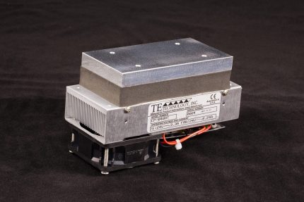 Three-quarter view of 67mm wide high temperature thermoelectric cold plate cooler/heater. Cooled aluminum plate on the front, waste heat exhausted to fins on back. Fins are fan cooled. The fan air enters on the back, off to one side, and exhausts on left and right. Operates on 24 volts DC and removes 40 watts of heat at a 0°C temperature difference relative to ambient. Can heat to 100°C without damaging the cooler. Internal extender blocks improve the capacity at larger temperature differences.